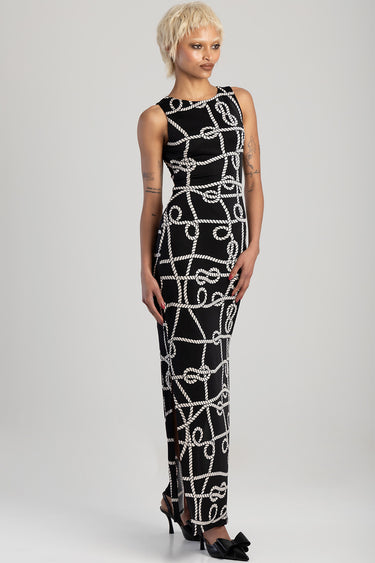 woman in a black sleeveless maxi dress with a white rope knot pattern, full length, standing in heels