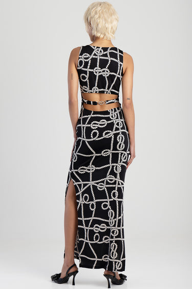 woman with short blonde hair wearing a black maxi dress with a white rope pattern seen from behind, cutout back and chain