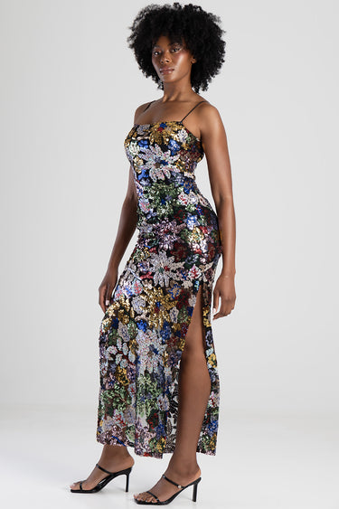 woman wearing a multicolour sequin floral maxi dress with thin straps side slit and black heeled sandals