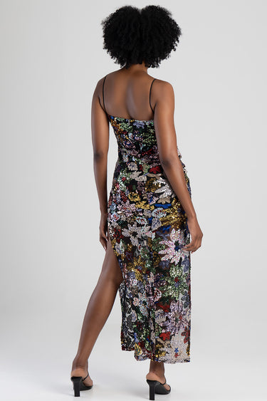woman wearing a multicolour sequin floral maxi dress with thin straps and a side slit, back view.