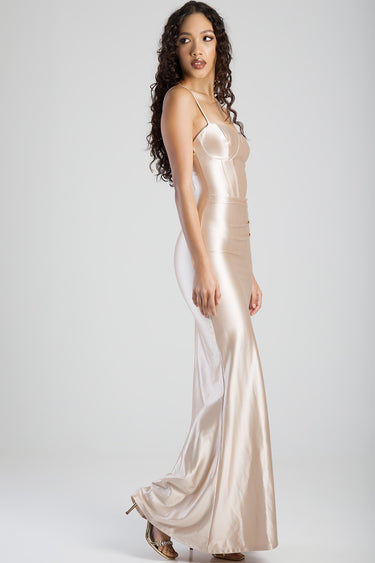 woman in a champagne satin corset dress with thin straps and a floor length skirt, seen in profile.