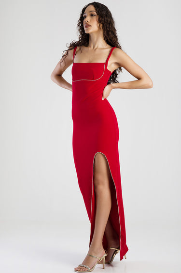 woman in a red maxi dress with delicate shoulder straps, silver trim, and a high slit, posing in gold heels.