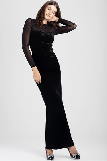 woman in a black velvet maxi dress with sheer long sleeves and ruched bodice, standing in heels
