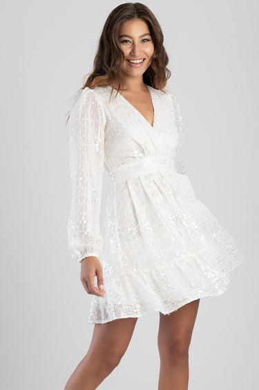 model in white sequin wrap dress with long sleeves and a tiered ruffle hem
