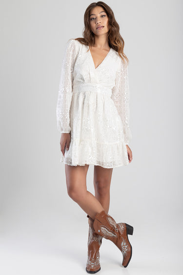 woman wearing a white long sleeve wrap dress with a belt and tiered skirt, paired with brown cowboy boots