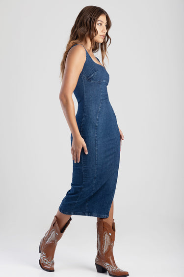 side view of a woman wearing a blue denim midi dress with spaghetti straps and brown western boots