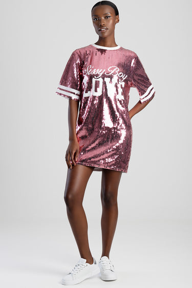 model wearing a pink sequined t shirt dress with white trim on the sleeves and neckline, paired with white sneakers