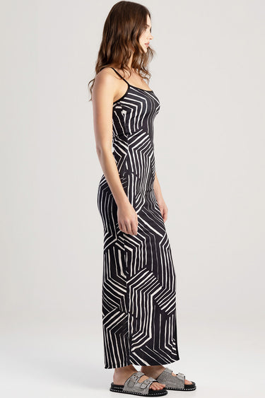 side view of a sleeveless maxi dress with a black and white geometric pattern on a model wearing silver sandals