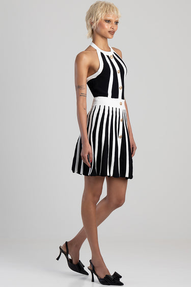 model wearing a black and white striped knit dress with halter neck, gold buttons, and a pleated skirt