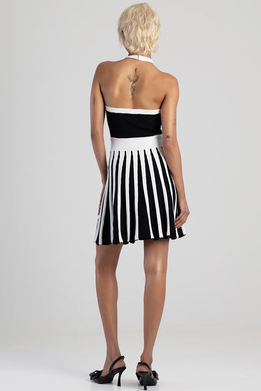 model wearing a black strapless top with white trim and a black and white pleated striped skirt, back view with heels