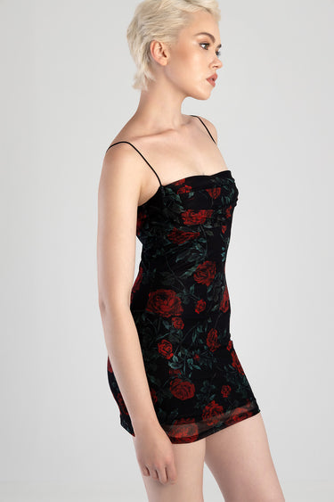 side profile of a woman wearing a black mini dress with red rose print, ruched bust, and thin spaghetti straps
