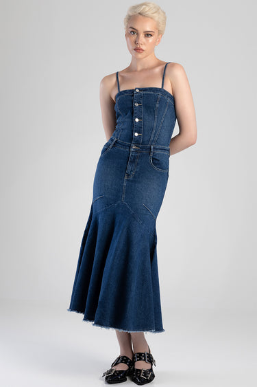 woman wearing a blue denim dress with thin straps, a buttoned bodice, fitted waist and a flared mid length hem with black
