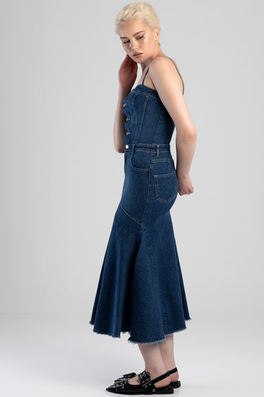 woman in a blue denim midi dress with spaghetti straps, button front bodice, fitted waist, flared hem and pockets, wearing