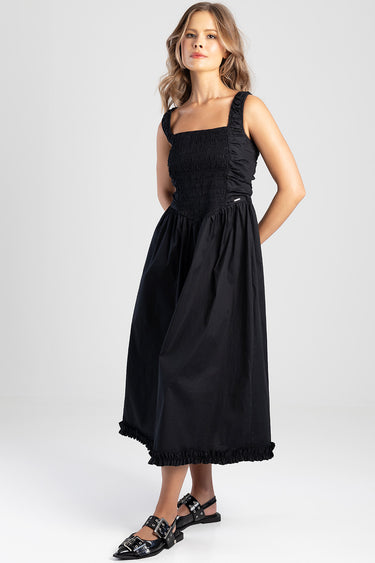 woman in a black midi dress with a smocked bodice and wide straps, a full gathered skirt with a ruffled hem, wearing black