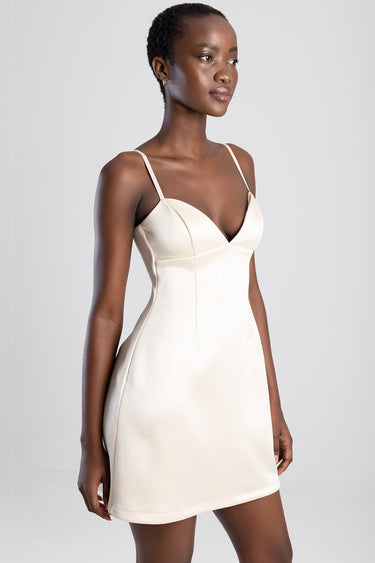 woman wearing a cream mini dress with spaghetti straps, v shaped neckline and fitted bodice, smooth flowing skirt