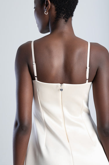 back view of a cream satin dress with thin straps and a small heart charm on the back zipper