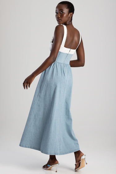 back view of a model in a light blue denim maxi dress with a white top and lace trim straps, wearing metallic heeled sandals