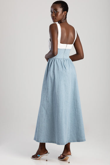 woman in a light blue denim maxi dress with a white bodice, back zipper, standing with her back turned