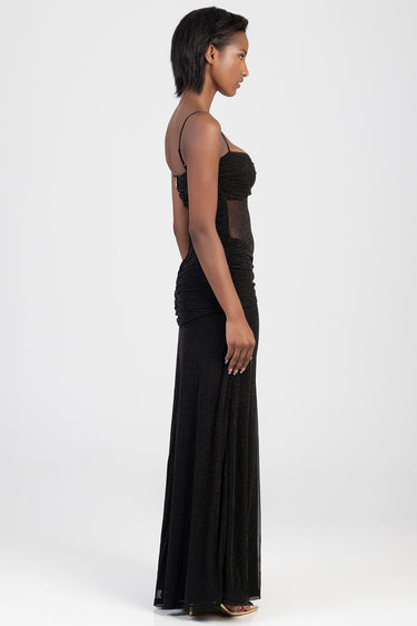 side view of a model in a black glittery maxi dress with spaghetti straps, ruched bodice and sheer panels.