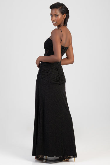 model wearing a black glittery maxi dress with thin straps, ruched bodice, and a flowing skirt in profile