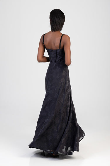back view of a woman in a navy blue maxi dress with floral jacquard, corset bodice and thin straps