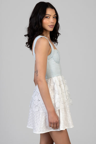 woman wearing a light blue denim dress with a sleeveless bodice and a white eyelet tiered skirt, side profile