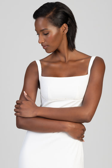 model wearing a white sleeveless maxi dress with square neckline and thin beaded straps, arms folded