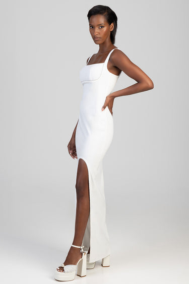 model wearing blue jean traders white sleeveless maxi dress with square neckline and side slit, paired with white platform