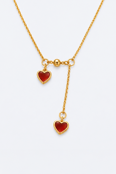gold tone necklace with two red heart charms, one fixed and one dangling on a lariat chain