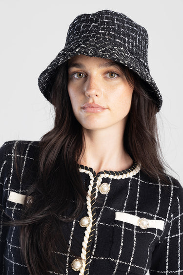 woman wearing a black and white tweed bucket hat and a black grid cardigan with pearl button trims