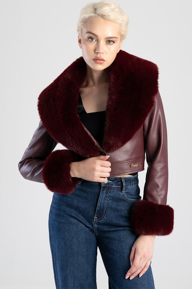 model wearing a burgundy faux fur jacket with an oversized collar and matching fur cuffs, paired with blue jeans visible in