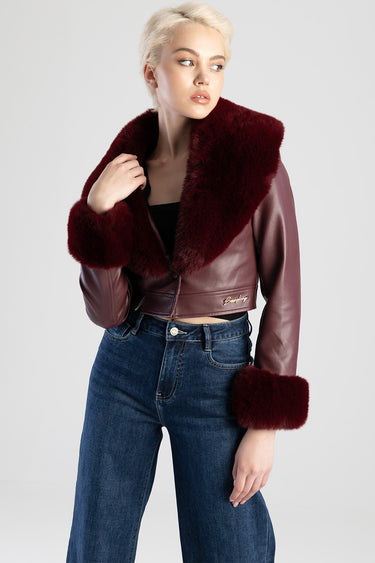 woman in a burgundy cropped leather jacket with a thick faux fur collar and fur cuffs, paired with blue denim jeans