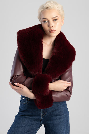 woman wearing burgundy faux fur jacket with a wide collar and matching cuffs over a black top and blue jeans.