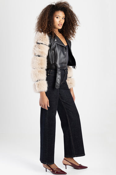 woman wearing black leather biker jacket with beige striped faux fur sleeves and dark wide leg jeans