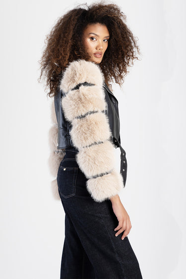 woman wearing a beige fur striped jacket over a black leather vest and dark denim jeans