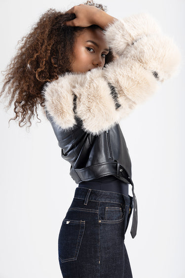 woman wearing a black leather biker jacket with large cream fur cuffs posing with arms raised