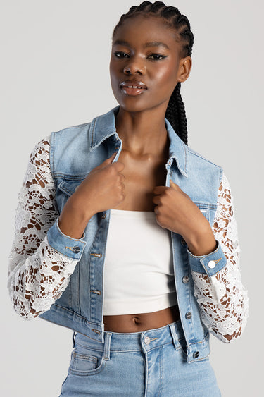 woman wearing a light wash denim jacket with white lace sleeves over a white crop top