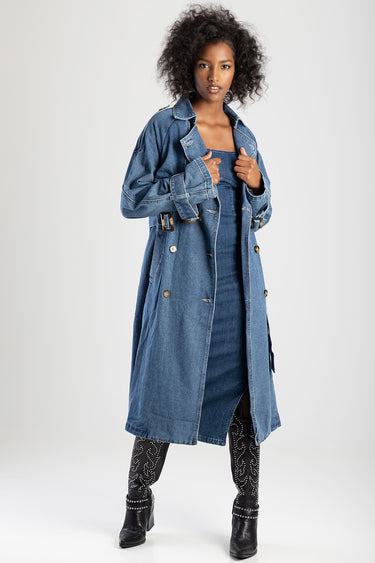 woman in a long blue denim trench coat with a buckle belt, paired with studded black leggings and heeled boots