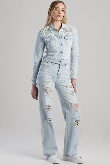 woman in a light wash denim jacket with pearl embellishments on the chest and pockets, distressed jeans and white sneakers