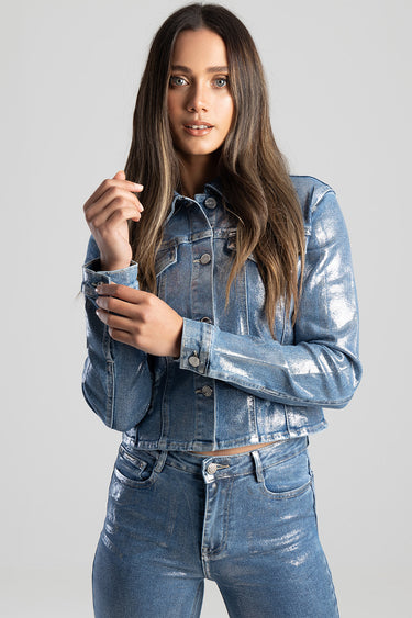 woman wearing a shiny blue denim jacket and matching jeans posing against a light gray background