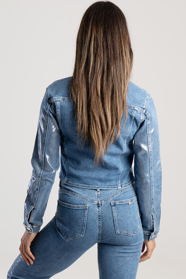 back view of a woman in a light wash denim jacket and matching jeans, long brown hair, subtle distressed fading on sleeves