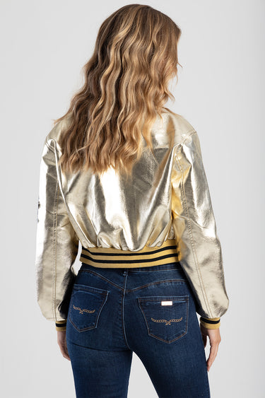 woman wearing a metallic gold bomber jacket with striped ribbed hem and cuffs, back view, paired with blue jeans