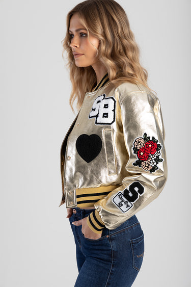 woman wearing a metallic gold bomber jacket with patches including a black heart a white number patch and floral sleeve