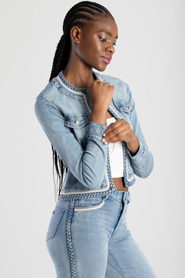 woman wearing a light blue denim jacket with braided trim and matching jeans, standing with hands at the collar