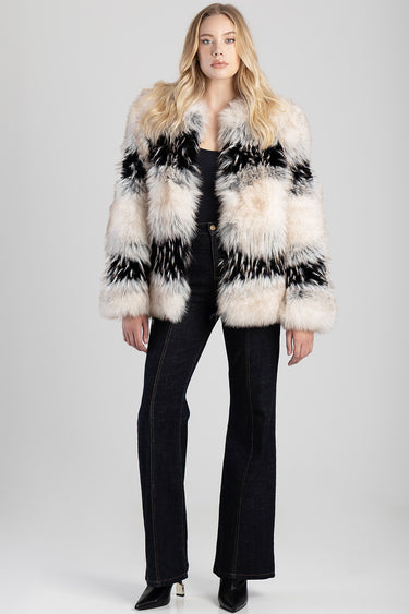 woman wearing a thick striped faux fur jacket in cream black and gray with dark jeans and black boots