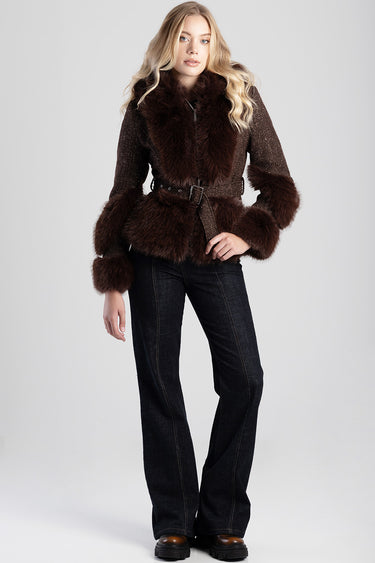 woman wearing a dark brown faux fur jacket with a wide collar and large cuffs, belted at the waist, paired with dark jeans