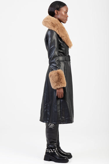 woman in a black leather long coat with tan fur collar and cuffs, belted at the waist, wearing black knee high boots with