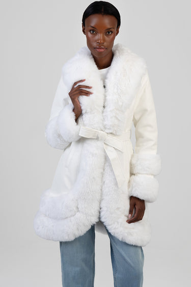 woman wearing a white faux fur trimmed coat with belt and wide lapels, paired with light blue jeans