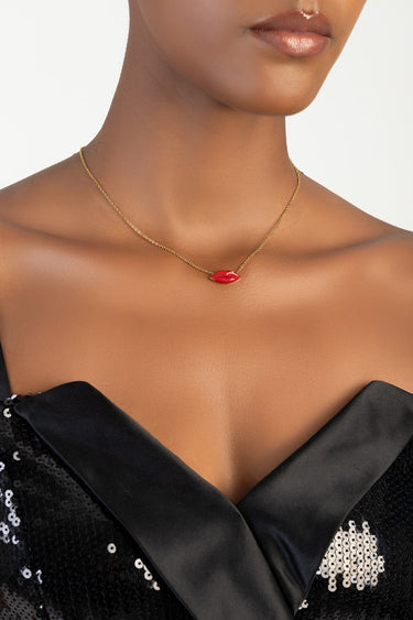 gold chain necklace with a red lip pendant worn on a model's neck over a black sequined top