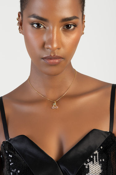 woman wearing a gold chain necklace with a pink cherry pendant against a black sequined dress